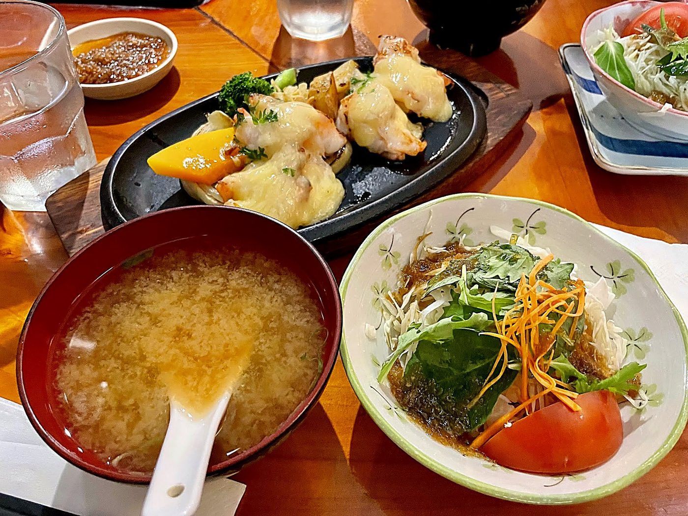 A teppanyaki set of fish fillet in yum yum sauce with grilled vegetables, beside a bowl of miso soup and a fresh green salad with tomato