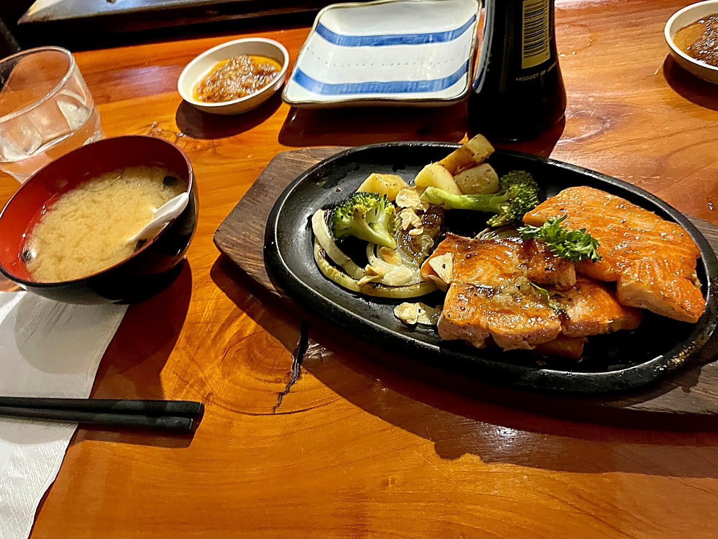 Salmon fillet and grilled courgette on a cast-iron plate on the wooden counter, with miso soup and a dipping dish alongside