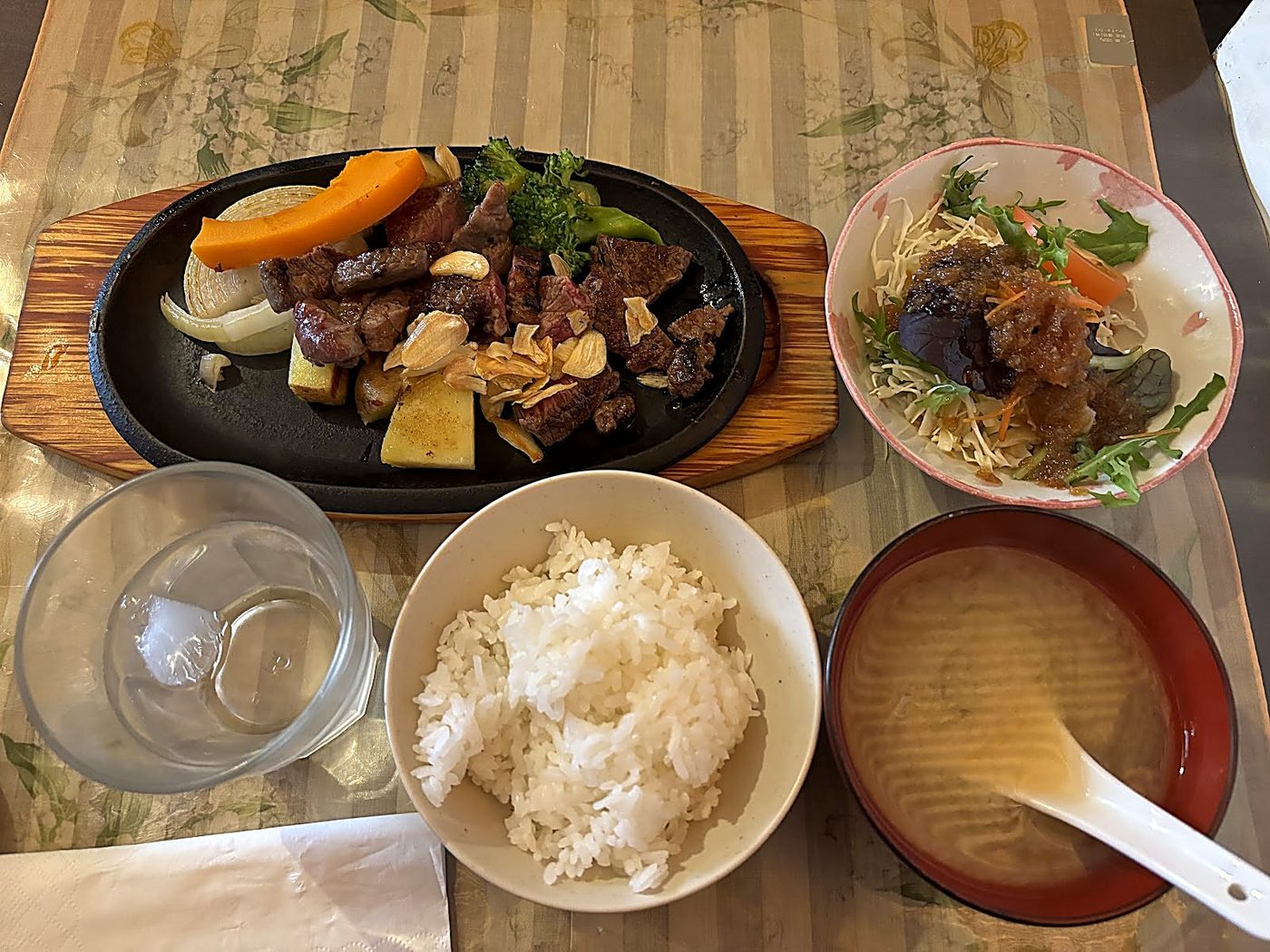 A teppanyaki steak set: sliced steak with grilled carrot, pumpkin and mushrooms on a cast-iron plate, with steamed rice, miso soup and salad